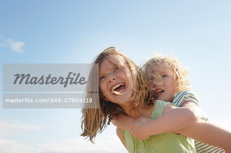 Low angle view of girl giving sister piggy back at coast