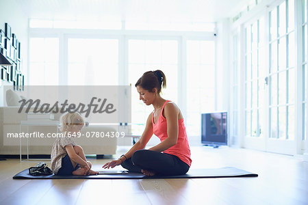 Mid adult mother and toddler daughter practicing yoga in living room