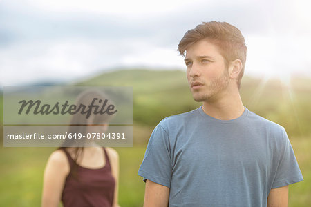Young couple standing apart and looking away in rural landscape under bright sunny sky