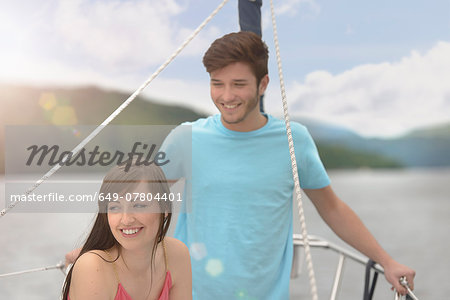 Young couple on bow of yacht sailing on lake under bright sunlight