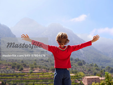 Rear view of boy looking at mountains with arms outstretched, Majorca, Spain