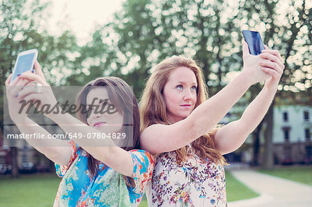 Two young female friends taking selfie on smartphones side by side