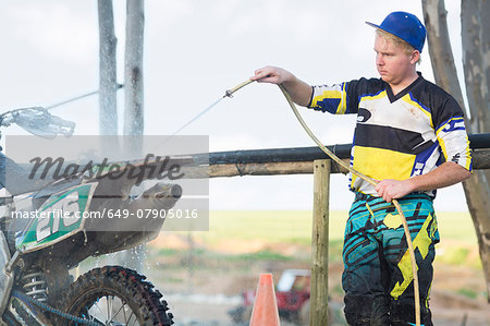 Young male motocross competitor cleaning motorcycle with water hose