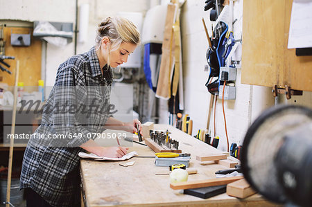 Young craftswoman making notes at workbench in pipe organ workshop