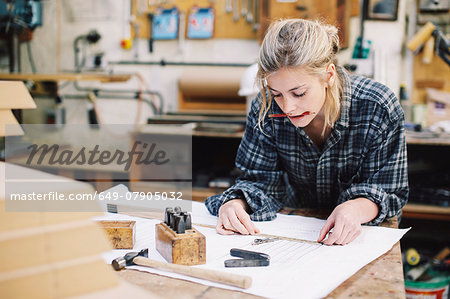 Young craftswoman measuring blueprint on workbench in pipe organ workshop