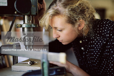 Young craftswoman drilling component in pipe organ workshop Young craftswoman drilling component in pipe organ workshop