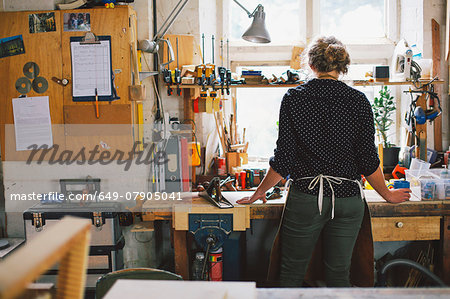 Rear view of young craftswoman at workbench in pipe organ workshop