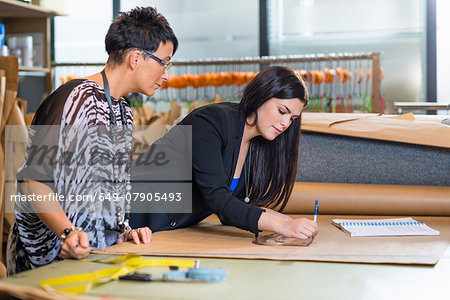 Two seamstresses drawing dressmakers pattern in workshop