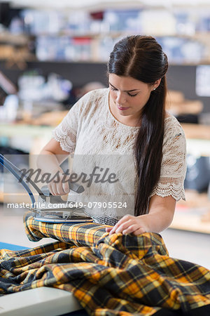 Young seamstress ironing tartan jacket in workshop