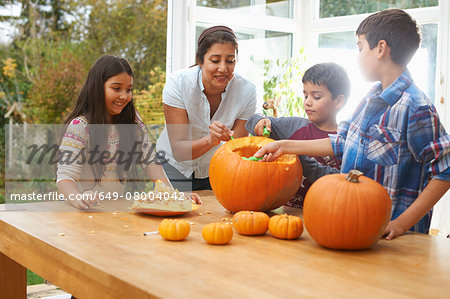 Mother and children carving pumpkin in dining room