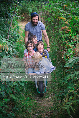 Mid adult man pushing wheelbarrow with smiling boys in garden