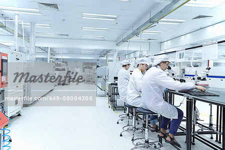 Workers using microscopes in factory that specialises in creating functional circuits on flexible surfaces