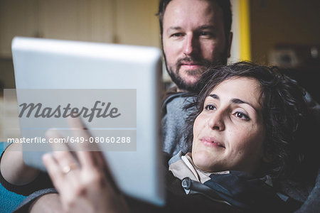Couple lying on sofa, using digital tablet