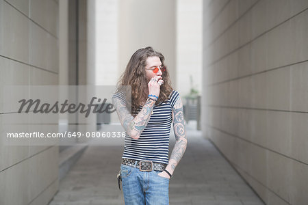 Young male hippy smoking cigarette in city alley