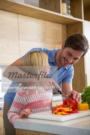 Man teaching daughter to slice vegetables on kitchen counter