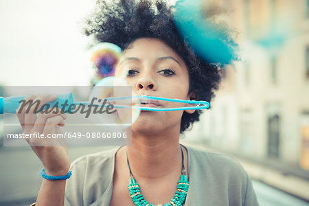 Portrait of young woman blowing bubbles with large wand