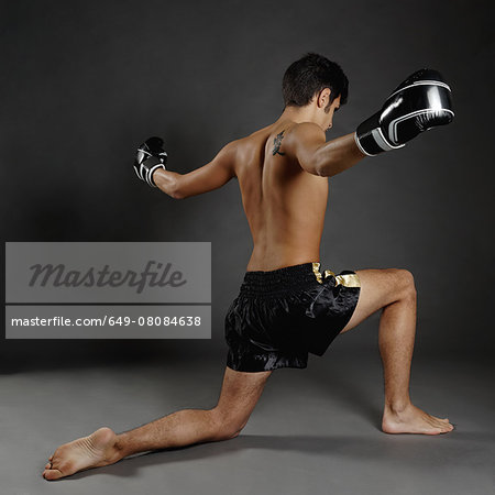 Rear view of young man in boxing gloves poised on one knee