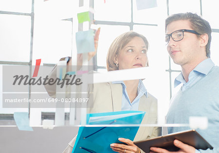 Businessman and woman pointing at idea notes on office glass wall