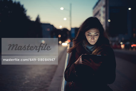 Mid adult woman using digital tablet on street at dusk Mid adult woman using digital tablet on street at dusk
