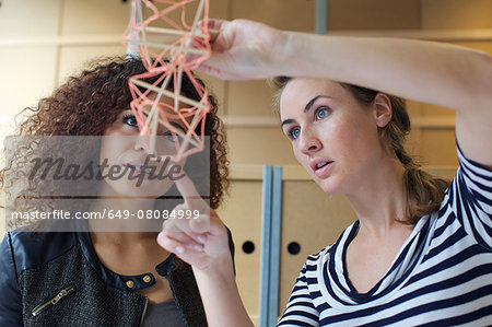 Two young female designers looking at handmade model in creative office