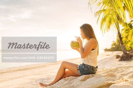 Young woman drinking fresh coconut milk on Anda beach, Bohol Province, Philippines