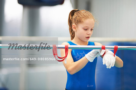 Young gymnast using training wrist straps to aid practise on bars