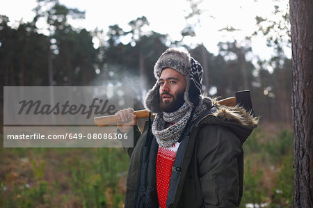 Young man carrying axe over his shoulder in forest