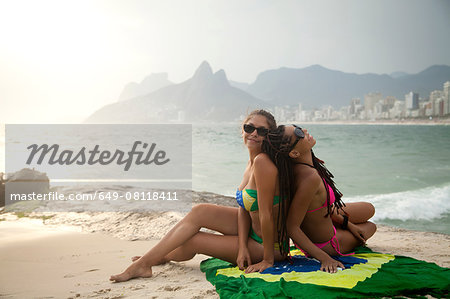 Portrait of two young women sitting on Brazilian flag,  Ipanema beach, Rio De Janeiro, Brazil