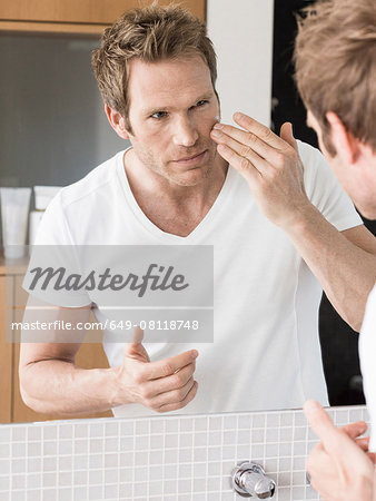 Mid adult man looking in bathroom mirror applying face cream