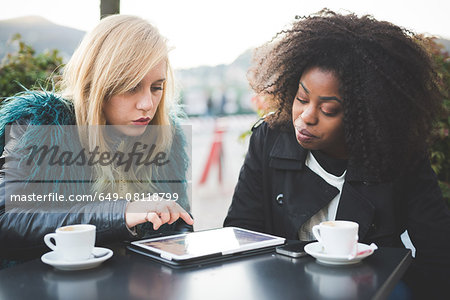 Two young women using touchscreen on digital tablet at sidewalk cafe, Lake Como, Como, Italy Two young women using touchscreen on digital tablet at sidewalk cafe, Lake Como, Como, Italy