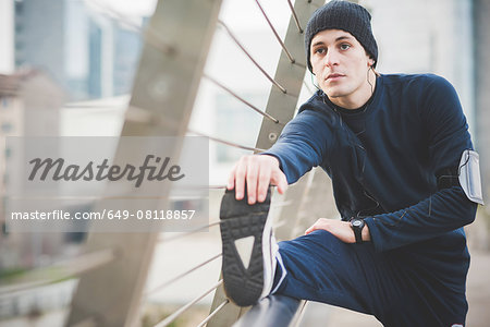 Young male runner touching toes on city footbridge