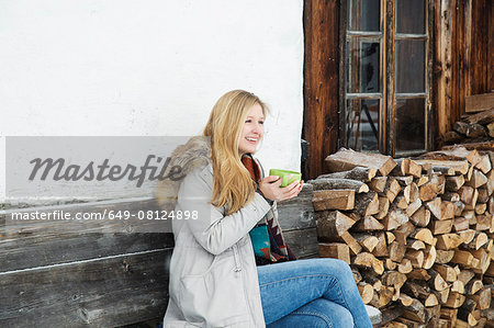 Young woman sitting outside wood cabin drinking coffee