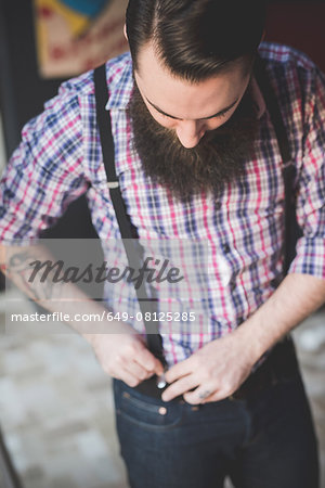 Young bearded man fastening braces onto jeans