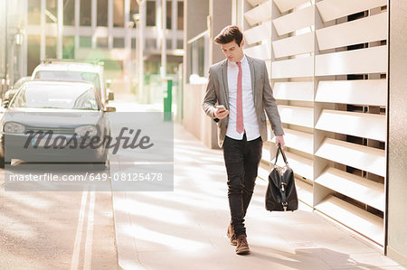 Young city businessman reading smartphone texts whilst walking outside office
