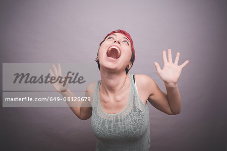 Studio portrait of young woman with short pink hair with hands raised