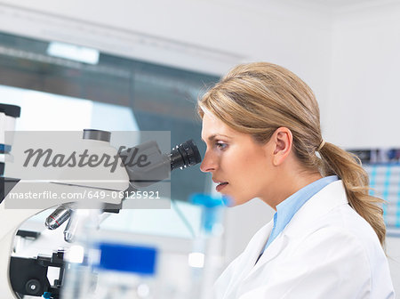 Scientist viewing sample on glass slide through microscope for medical testing