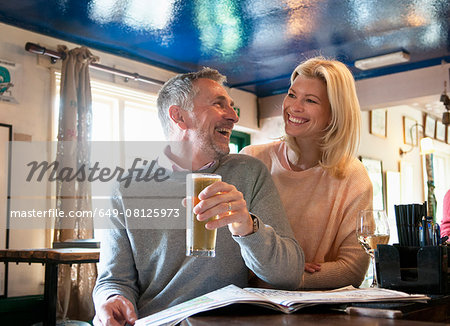 Couple laughing and reading newspaper in pub Couple laughing and reading newspaper in pub