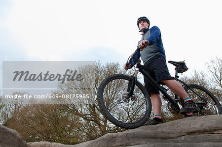Mature male mountain biker looking out from rock formation