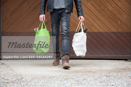 Teenage boy carrying reusable shopping bags full of empty bottles for recycling