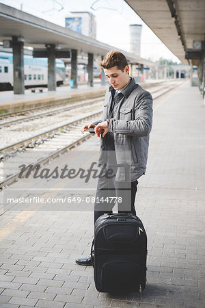 Portrait of young businessman commuter checking wristwatch for the time at train station.
