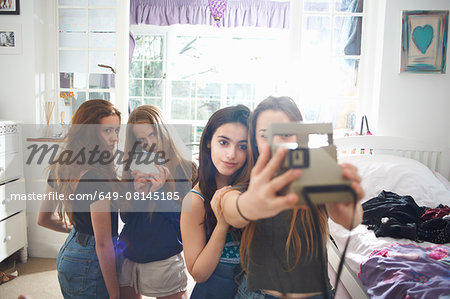 Four teenage girls in bedroom taking instant camera selfie