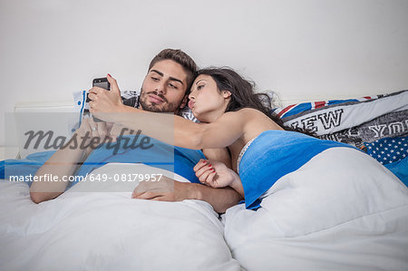 Young couple taking smartphone selfie in bed