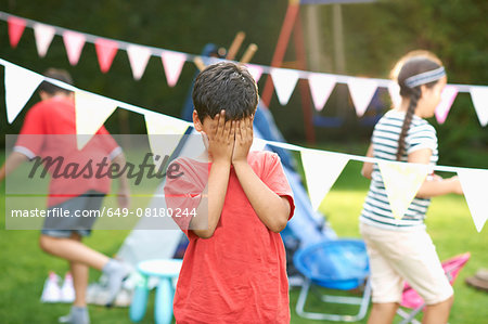 Boy covering his eyes for hide and seek with brother and sister in garden