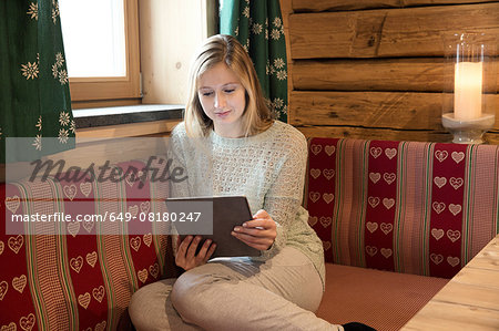 Young woman reading digital tablet in log cabin