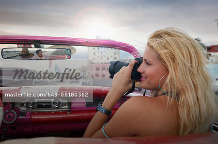 Young woman taking pictures from a vintage car on the Havana' Malecon, Cuba