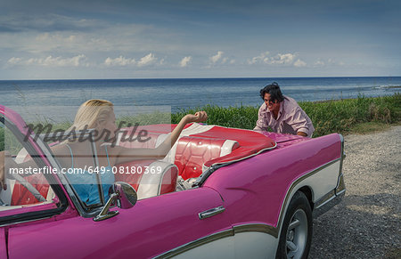 Young man pushing pink vintage convertible at coast whilst girlfriend drives, Havana, Cuba