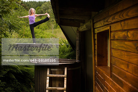 Mature woman practicing yoga pose on footbridge at eco lodge