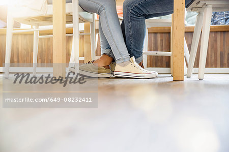 Surface level view of couples entwined legs sitting at table face to face