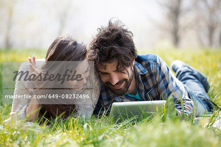 Young couple on picnic blanket browsing digital tablet