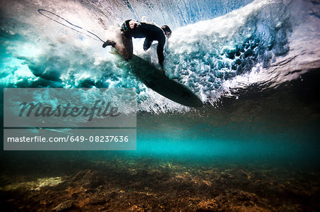 Underwater view of surfer falling through water after catching a wave on a shallow reef in Bali, Indonesia